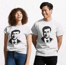 a man and a woman are standing next to each other wearing t-shirts with a picture of a man on them .