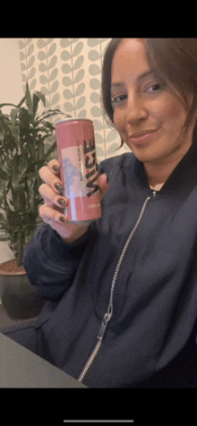 a woman in a blue jacket holds a can of vice