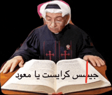 a man is sitting at a table reading a bible with arabic writing on it