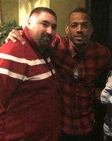 two men are posing for a picture together in a room . one of the men is wearing a plaid shirt .