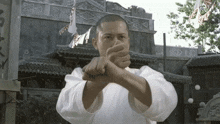 a man in a white karate uniform holds his fist up in front of a building with chinese writing on it