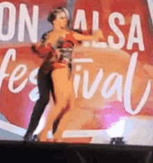 a man and a woman are dancing on a stage in front of a sign that says salsa festival .