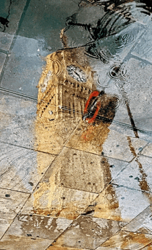 a reflection of big ben is seen in a puddle of water