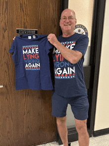 a man holds up a blue shirt that says make lying wrong again