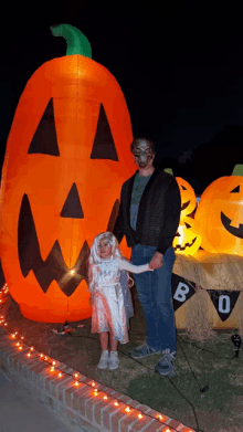 a man and a little girl are standing in front of an inflatable pumpkin that says boo