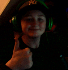 a young man wearing headphones and a ny hat gives a thumbs up