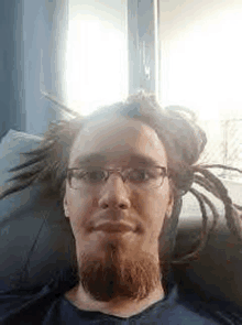 a man with dreadlocks and glasses is laying on a couch and looking at the camera .