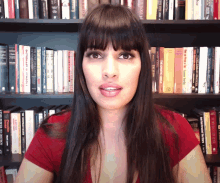 a woman in a red shirt stands in front of a bookshelf filled with books including one titled " the greatest comeback "