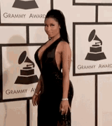 a woman in a black dress is standing on a red carpet in front of a grammy award sign .