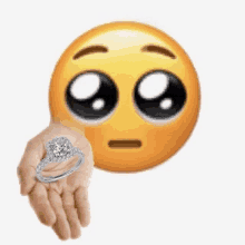 a person is holding a diamond ring in their hand in front of an emoji .