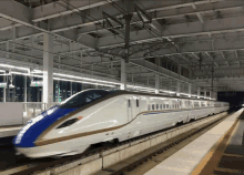 a white and blue bullet train is pulling into a train station