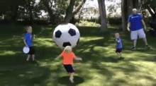 a group of children are playing with a large inflatable soccer ball in a park .