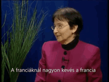 a woman wearing glasses and a pink jacket is talking in a video in a language other than english