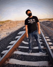 a man wearing a black shirt that says lacoste stands on train tracks