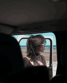 a woman wearing sunglasses looks out a car window at the beach