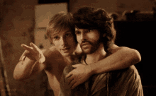 two shirtless men are hugging each other in a dark room