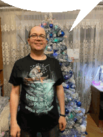 a man wearing a black t-shirt with a fisherman on it stands in front of a decorated christmas tree