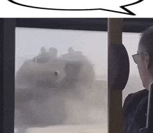 a man sitting on a bus looking out a window at a military vehicle