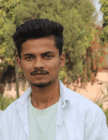 a young man with a beard wearing a white shirt looks at the camera