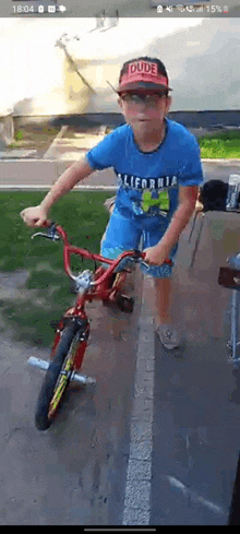 a young boy wearing a blue shirt and a red hat is riding a red bicycle .