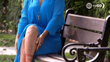 a woman in a blue dress is sitting on a wooden bench .