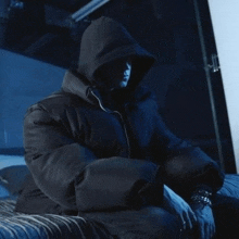 a person wearing a hooded jacket is sitting on a bed in the dark .