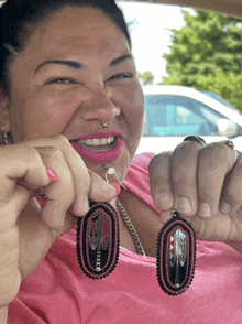 a woman in a pink shirt is holding a pair of red and black earrings