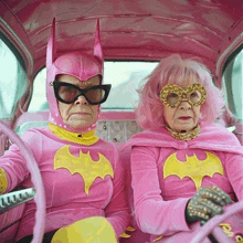 two women dressed in pink batman costumes are sitting in a car