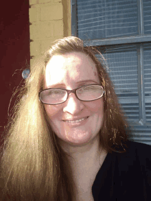 a woman wearing glasses is smiling in front of a window with blinds