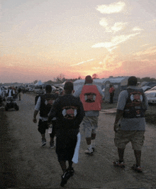 a group of men are walking down a dirt road with one wearing a t-shirt that says " biker " on it