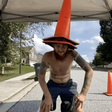 a shirtless man wearing an orange traffic cone hat