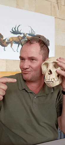 a man in a green shirt is holding a skull and pointing