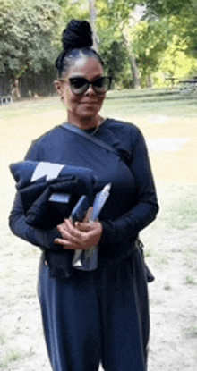 a woman wearing sunglasses and a black shirt is holding a blanket and a bottle of water .