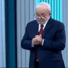 a man in a suit and tie is praying with his hands folded in front of a blue curtain .