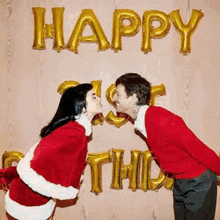 a man and a woman are kissing in front of a wall with balloons that say happy first christmas .