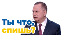 a man in a suit and tie is talking into a microphone with the words " ты что " in blue and yellow behind him