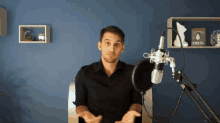 a man in a black shirt stands in front of a microphone with a book on the shelf behind him titled emmys