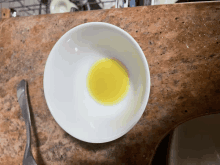 a white bowl with a yellow liquid in it sits on a granite counter top