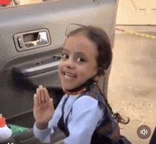 a little girl is sitting in the back of a car waving