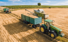 a green john deere tractor is pulling a trailer full of wheat