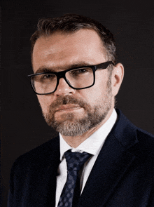 a man with glasses and a beard wearing a suit and tie