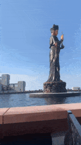 a statue of a woman standing in front of a body of water with a blue sky in the background