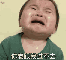 a baby in a green shirt is crying with chinese writing on his face .