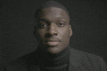 a man wearing a black turtleneck and a black suit looks at the camera