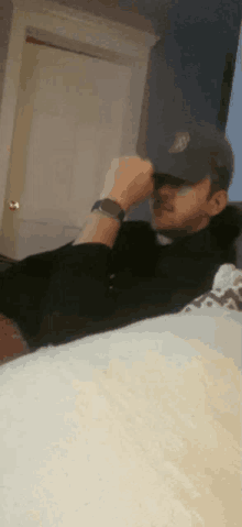 a man wearing a hat and a watch is laying down on a bed