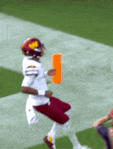 a football player in a red and white uniform is jumping in the air while holding an orange object .