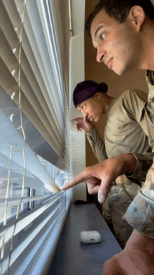 two men are looking out a window with blinds