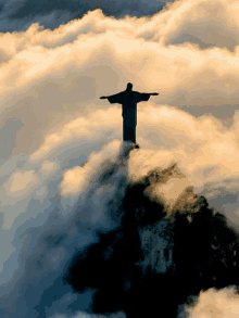 a statue of jesus is surrounded by clouds on top of a hill