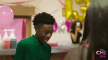 a boy in a green shirt is talking to a woman in a room with balloons and a sign that says " the chi "