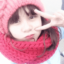 a girl wearing a pink hat and a red scarf is giving a peace sign